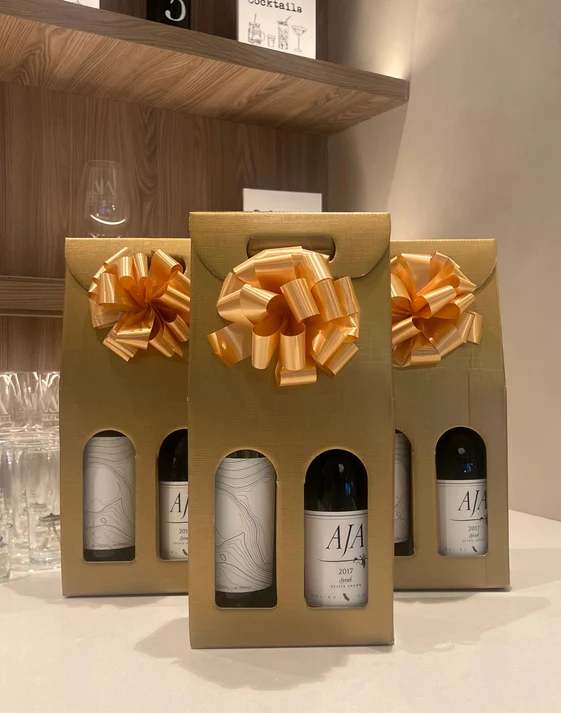 Gold two-bottle gift carriers with bows lined up on a shelf