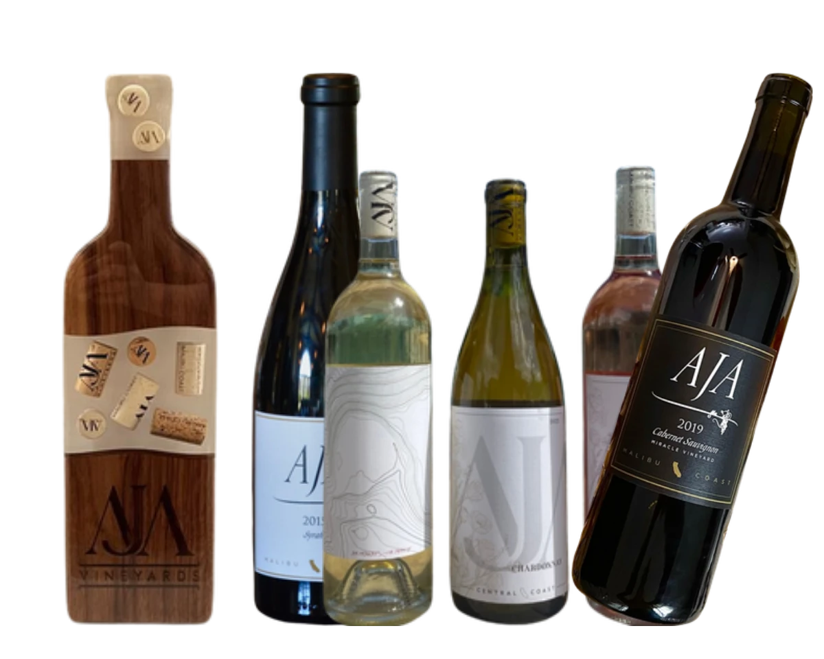 A custom AJA wood charcuterie board beside three bottles of AJA wine